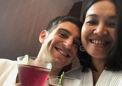 honeymoon couple travelers wearing white bathrobes with purple butterfly pea cocktails in their hotel room