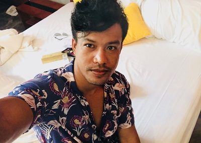 solo traveler wearing a tropical shirt taking a selfie sitting on the Butterfly Pea hotel room bed after reading a book