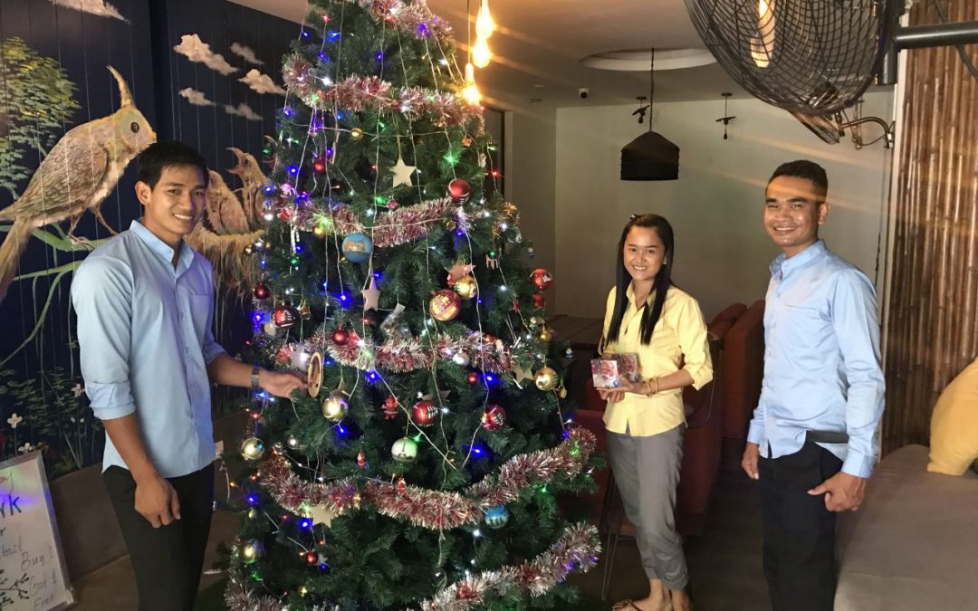 Three Butterfly Pea staff members standing around a Chrsitmas tree in Siem Reap, Cambodia